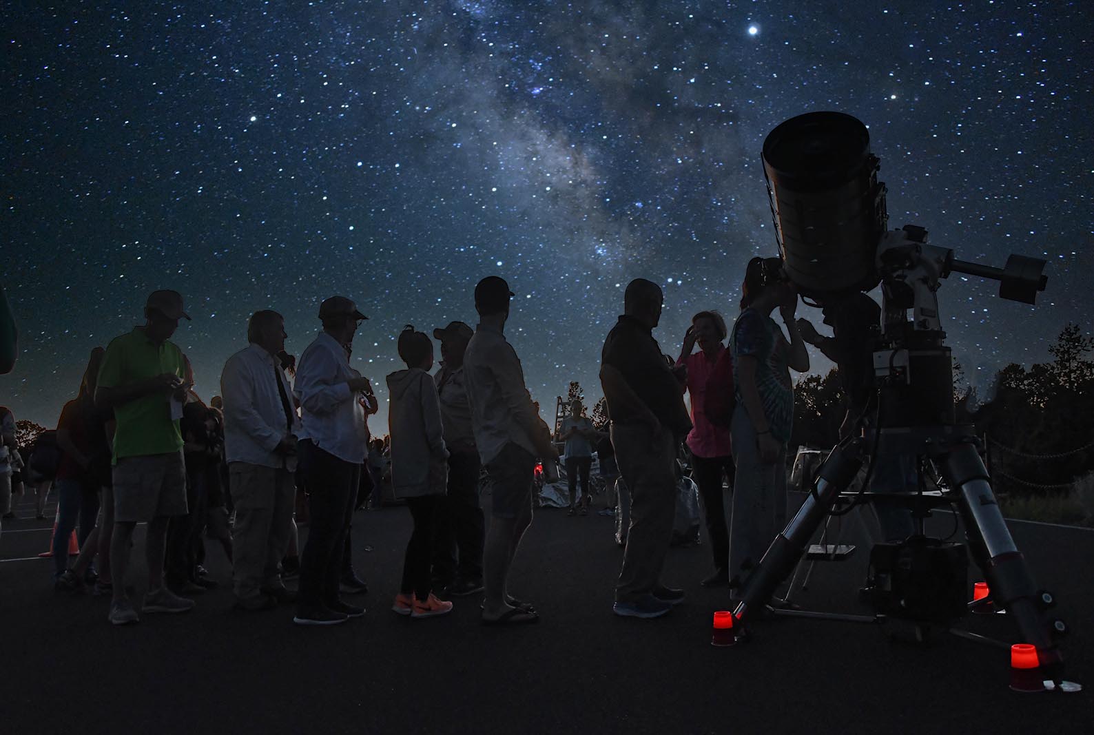 A group of people gather around a telescope with the night sky above