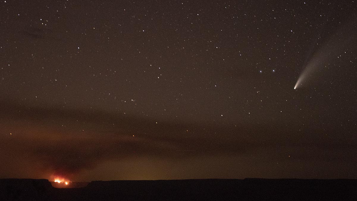 at night, a distant fire is seen burning on the horizon with a layer of smoke in the starry sky above. On the left, a comet with a long tail.