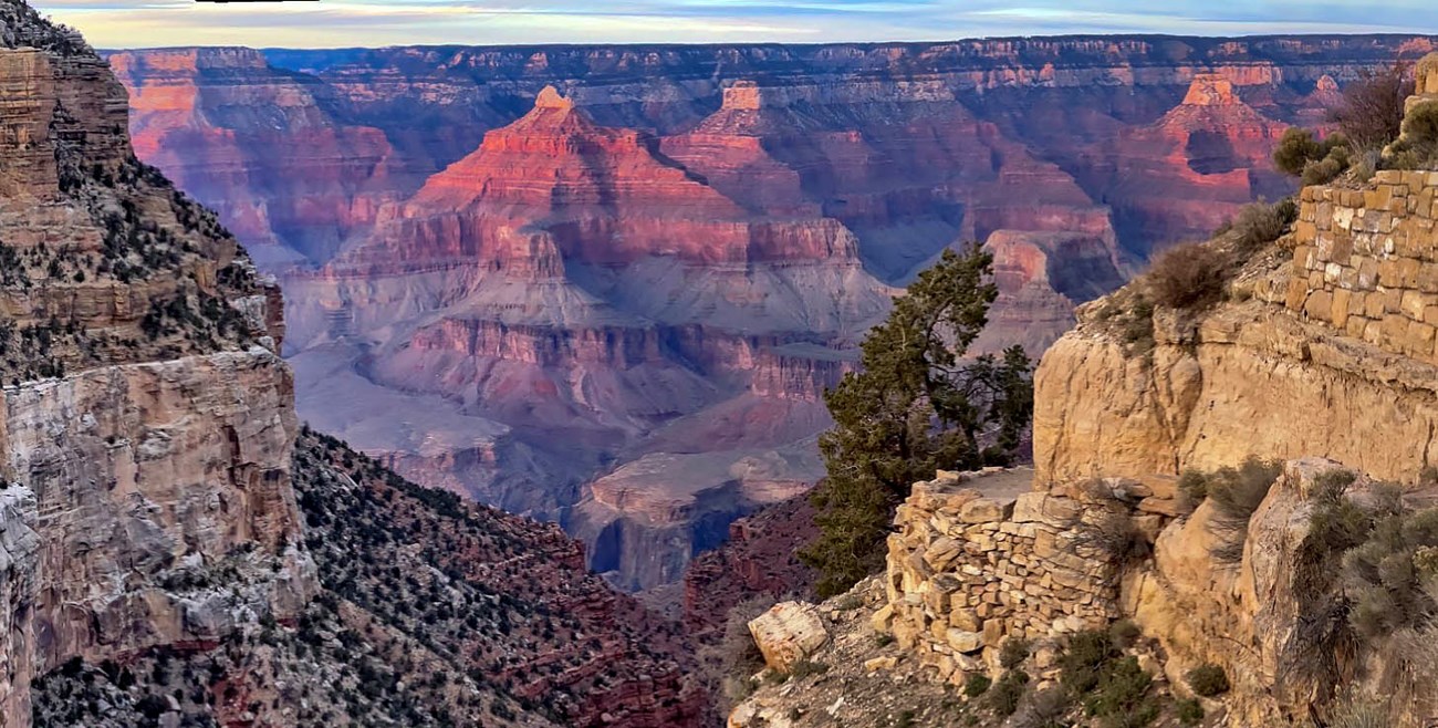 Looking between a "v" formed by slopes and cliffs on both sides, towards distant peaks bathed in pink sunset light.