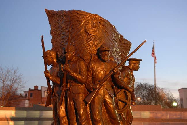 A bronze statue of African American Civil War soldiers holding guns at dusk