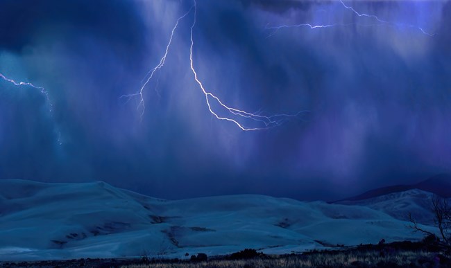 Lightning bolts strike the dunes under a dark sky