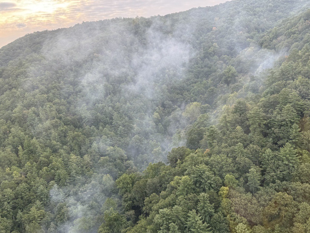 Aerial view of plumes of smoke rising from between lush, rolling mountain ridges.