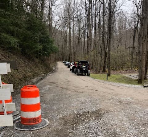 Gravel road with traffic cones on left and vehicles parked along the road on the right side.