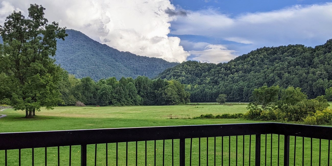 Rolling mountains in the background of a large, grassy field. Porch railing in foreground.