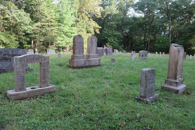Multiple headstones in a National Park Service cemetery. Green trees in the background.