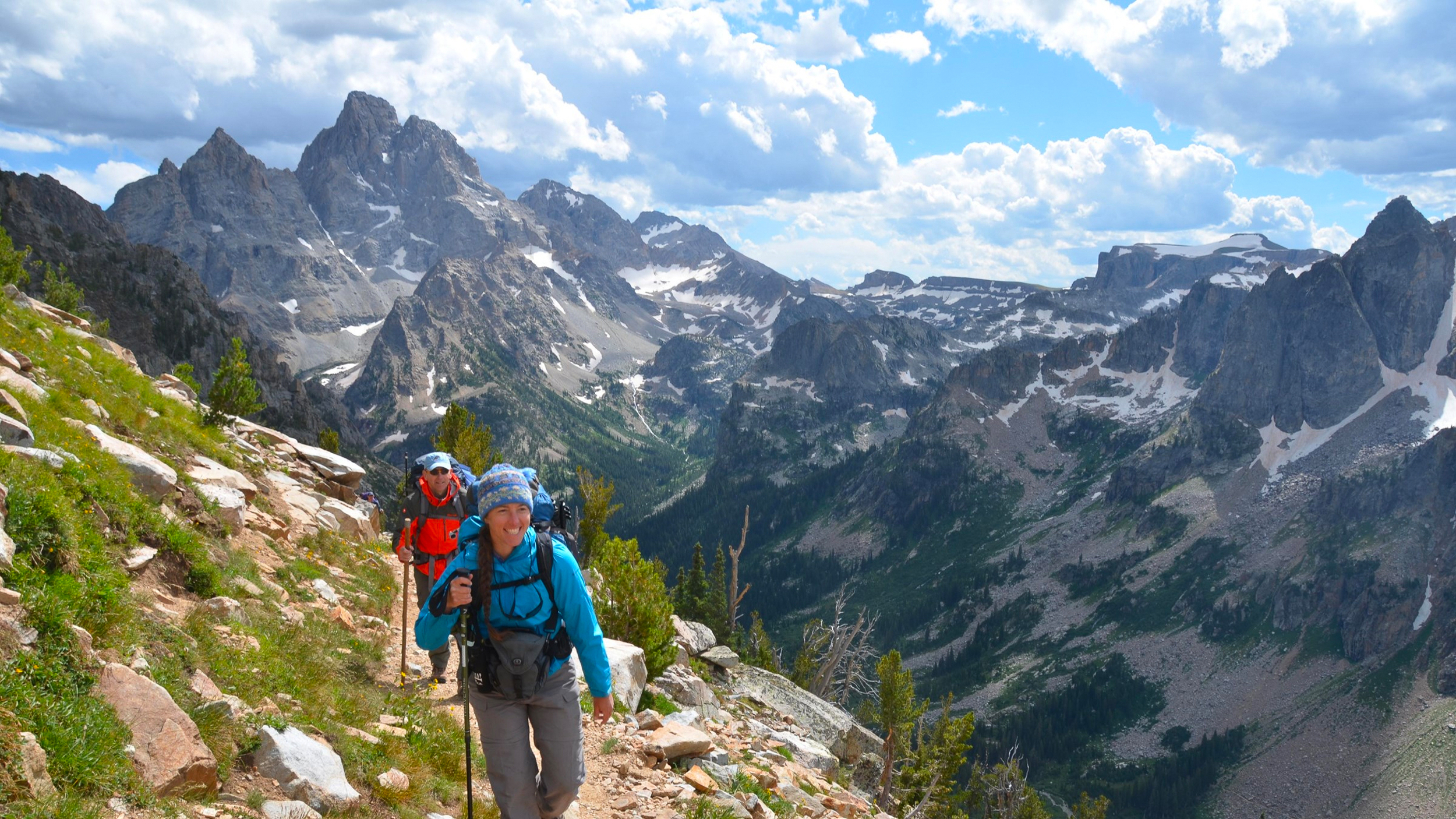 Two hikers walking up a mountain divide with mountains and a canyon behind