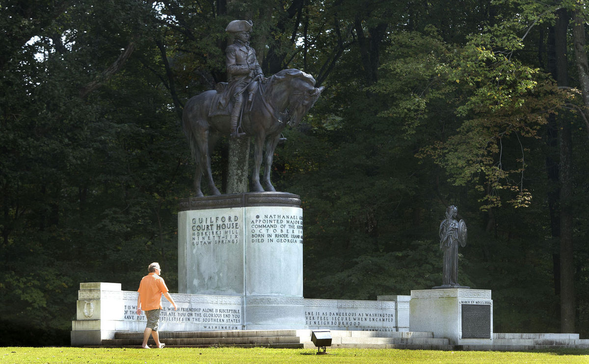 Man in orange shirt walks in front of the equestrian monument to Maj. General Nathanael Greene