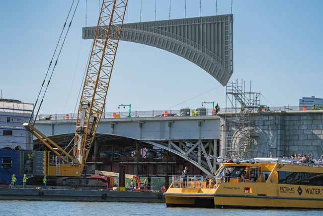 Crane lifts large piece of steel for installation on side of Arlington Memorial Bridge