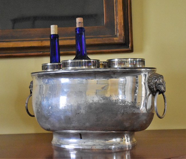 A silver, four-bay wine cooler with two bottles, set on a side table.