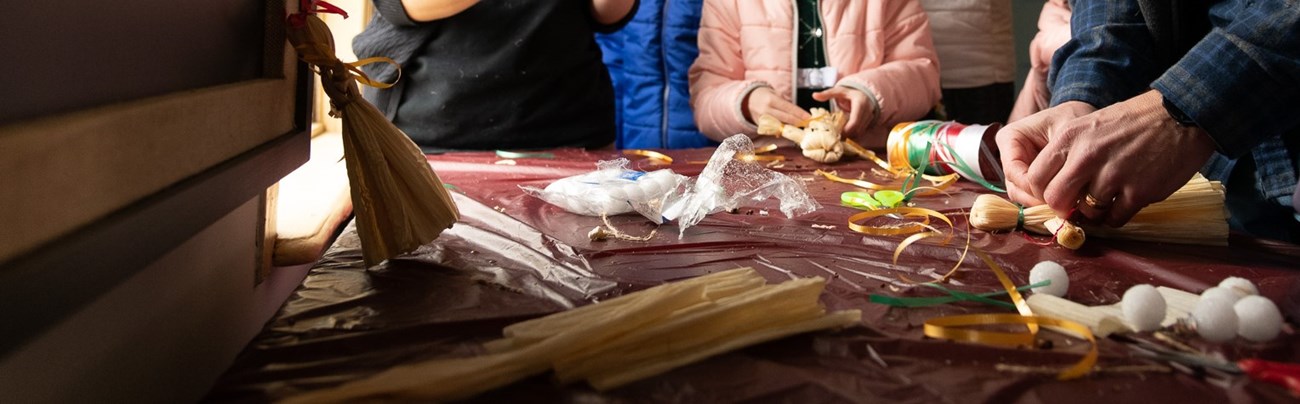 Members of the public making cornhusk dolls out of various materials on a table.