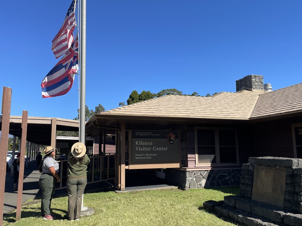 Two park rangers raise the flags outside a visitor center