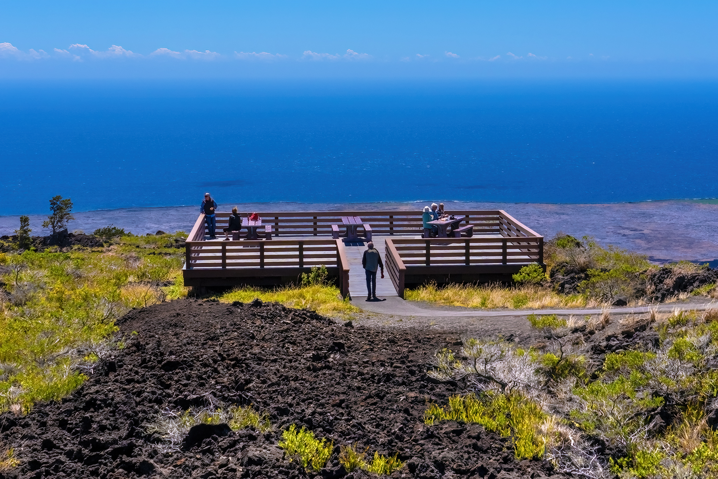 Wooden deck overlooking coastline with six people and picnic tables