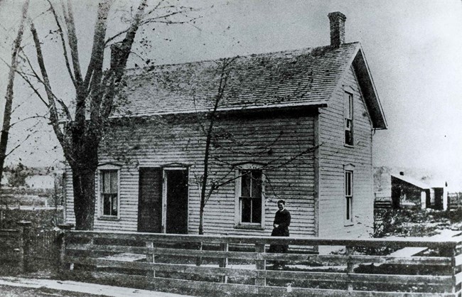 An 1880s photo shows a woman standing in the yard of her two story house.