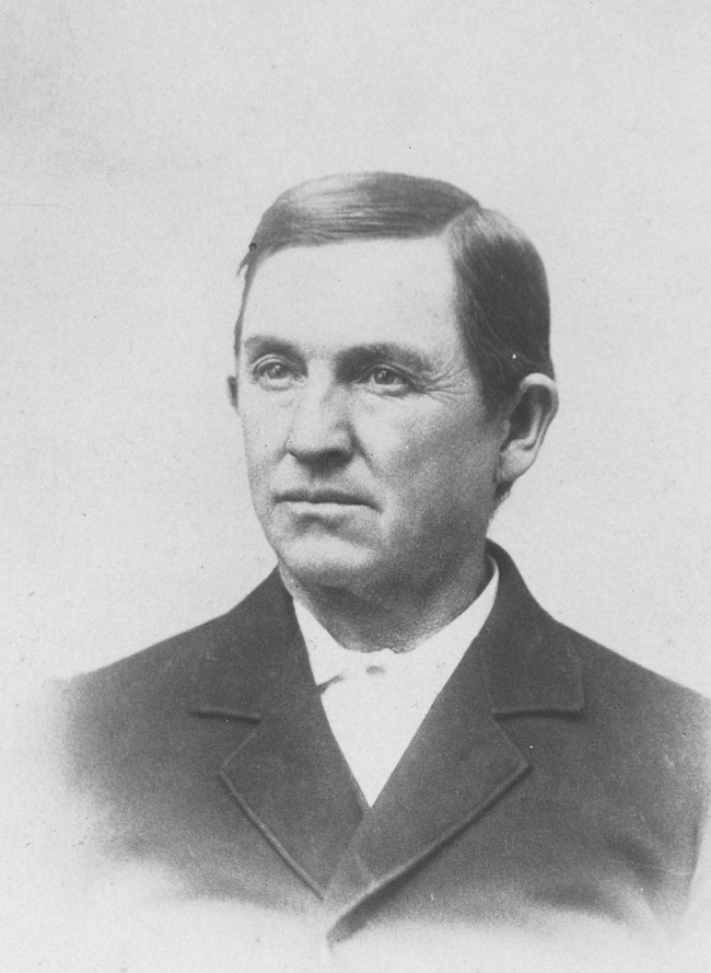 An 1800s portrait photo depicts a clean shaven man with a shirt collar and jacket.
