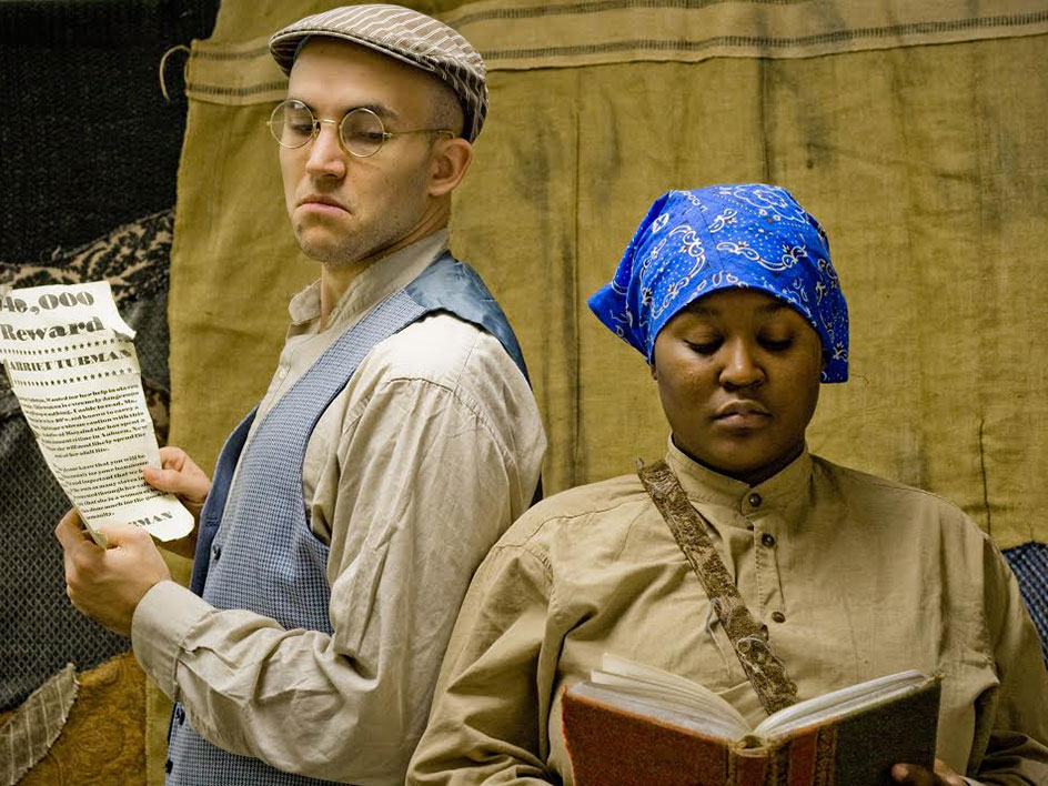 Stage actors in 19th century dress portray a white man and a black woman.