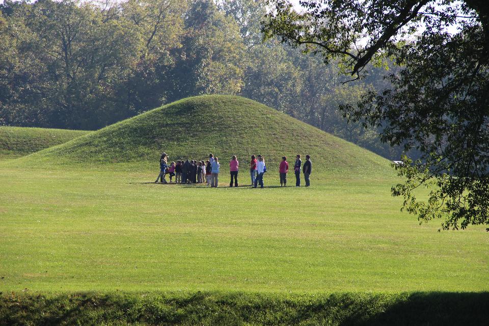 A ranger on the left speaks to several people in front of grass covered mounds