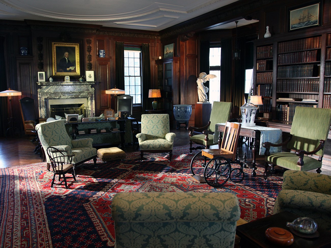 A large room lined with bookshelves and crowded with furniture.