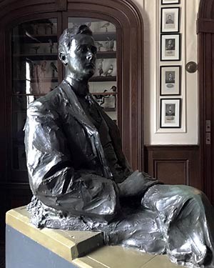 A bronze statue of a man (FDR) in a room surrounded by prints and mounted birds.