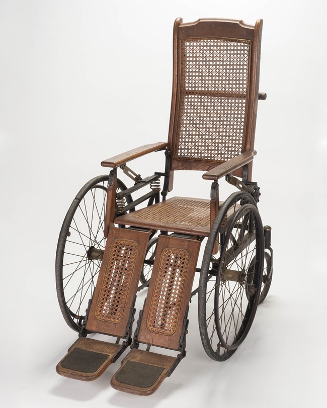 A wood wheelchair with caned seat, back, and leg rests