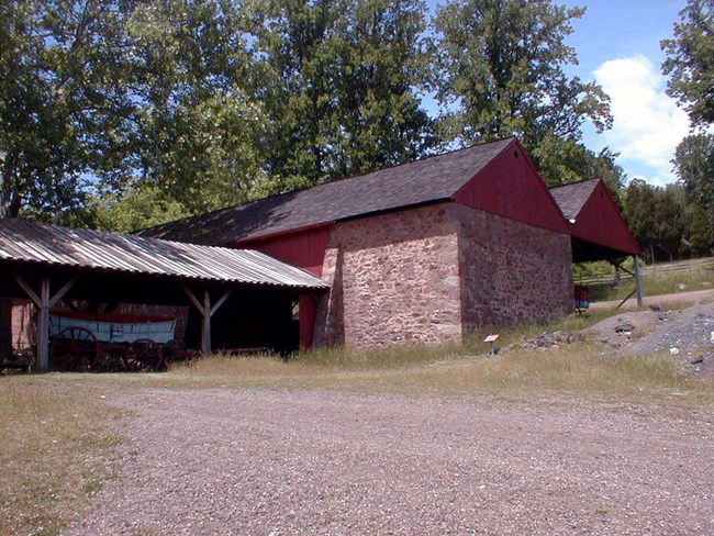Stone building with red gable. Shed built on behind the house. Wagon sits in front of house.