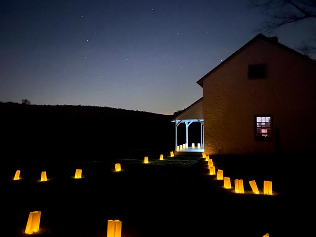 Lantern lit path leads to a building, it is night and there are stars out.
