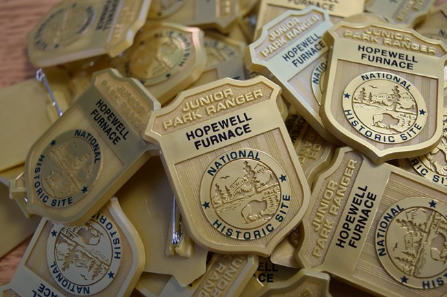 Pile of gold Junior Ranger badges that read Hopewell Furnace.