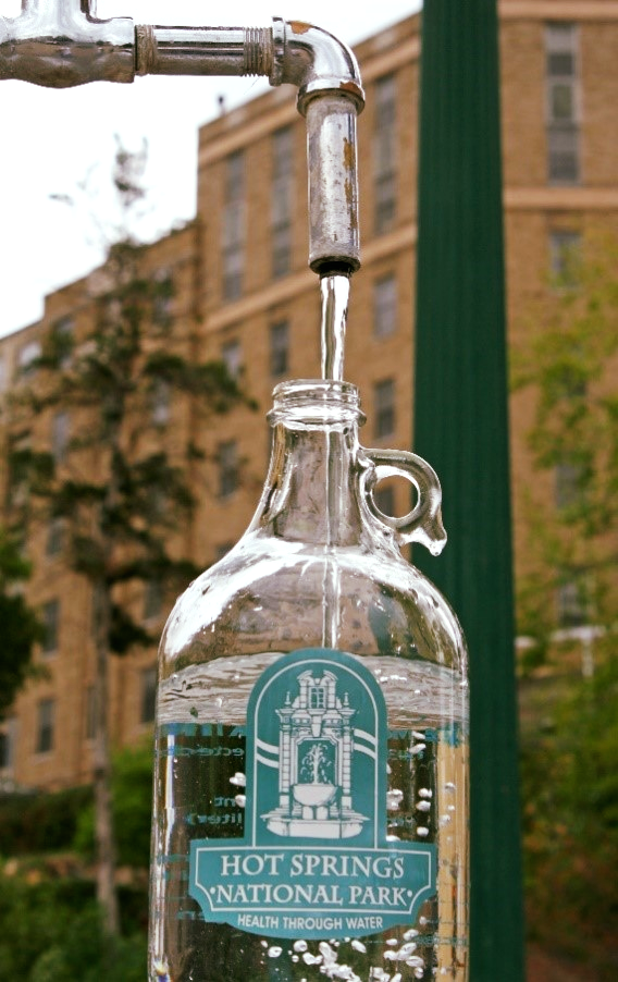 A glass bottle with the Hot Springs National Park logo on it is filled by thermal water at one of the fountains.