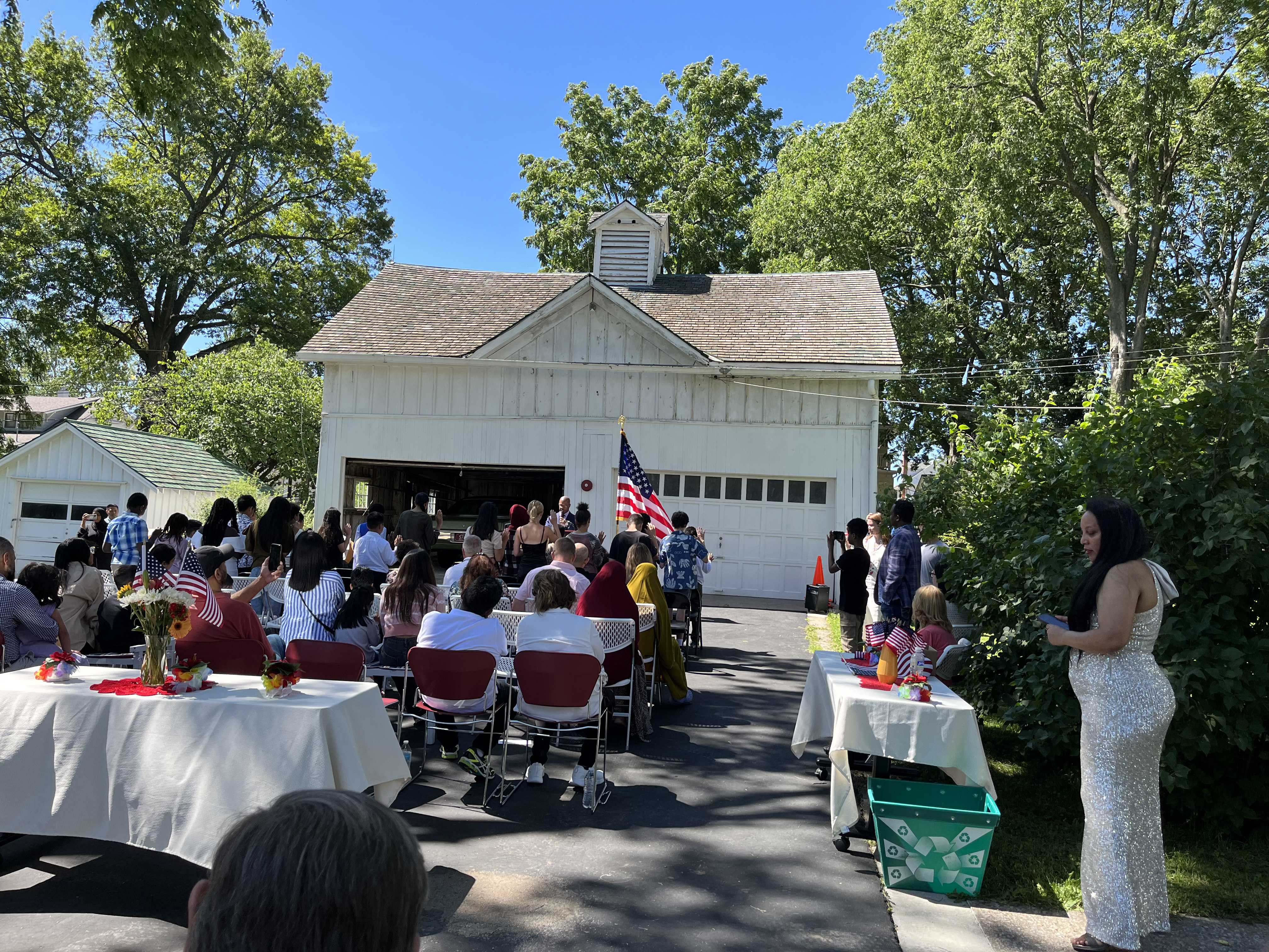 A group of young new citizens stand with their right hands raised, families nearby, with the American flag close. President Truman's car is housed in his garage.