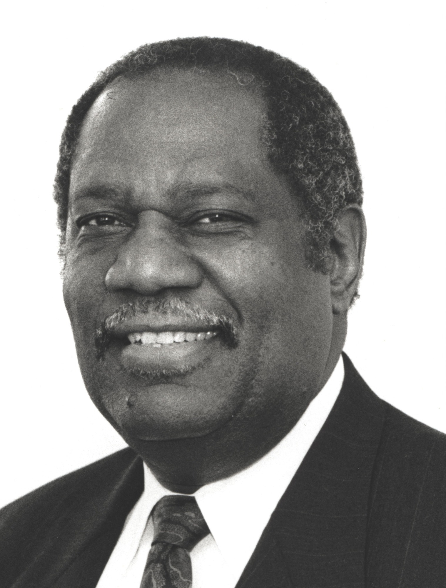 Head shot of smiling Black man in suit and tie.