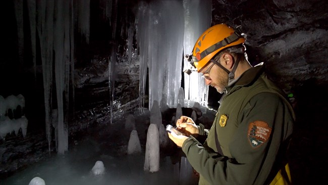 Field technician inside a cave entering data on hand held device with ice in background