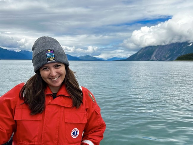 Sofia Elizarraras, Ecology Assistant Woman in bright red winter coat in open boat on the water with mountains in the distance