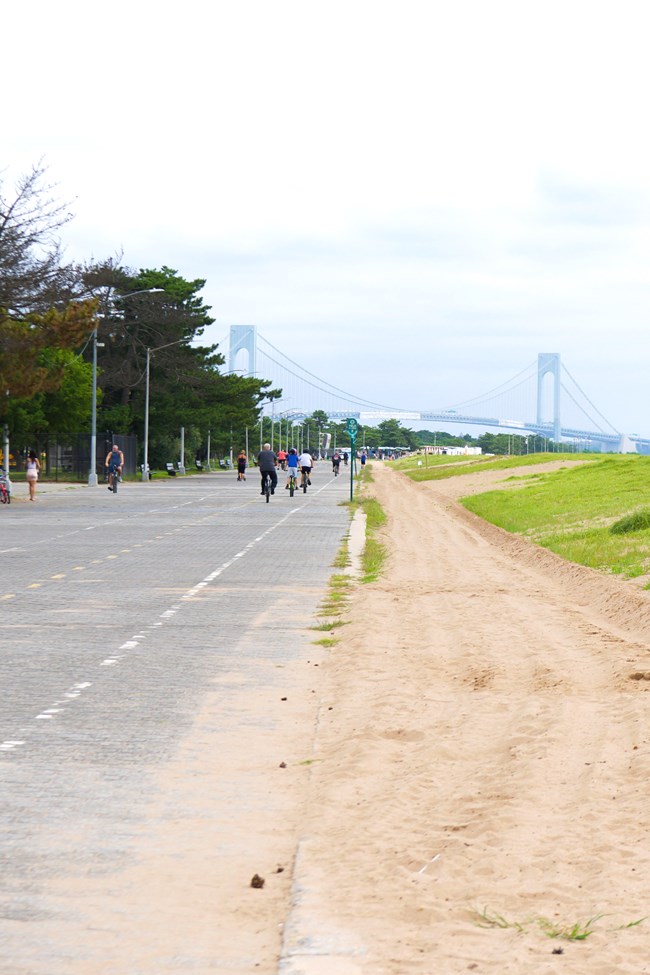A bike path along sand dunes and beach with a bridge in the background