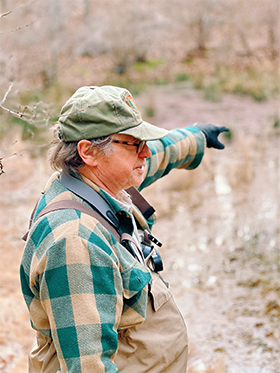 Scientist stands in waders and points to something in a vernal pool.