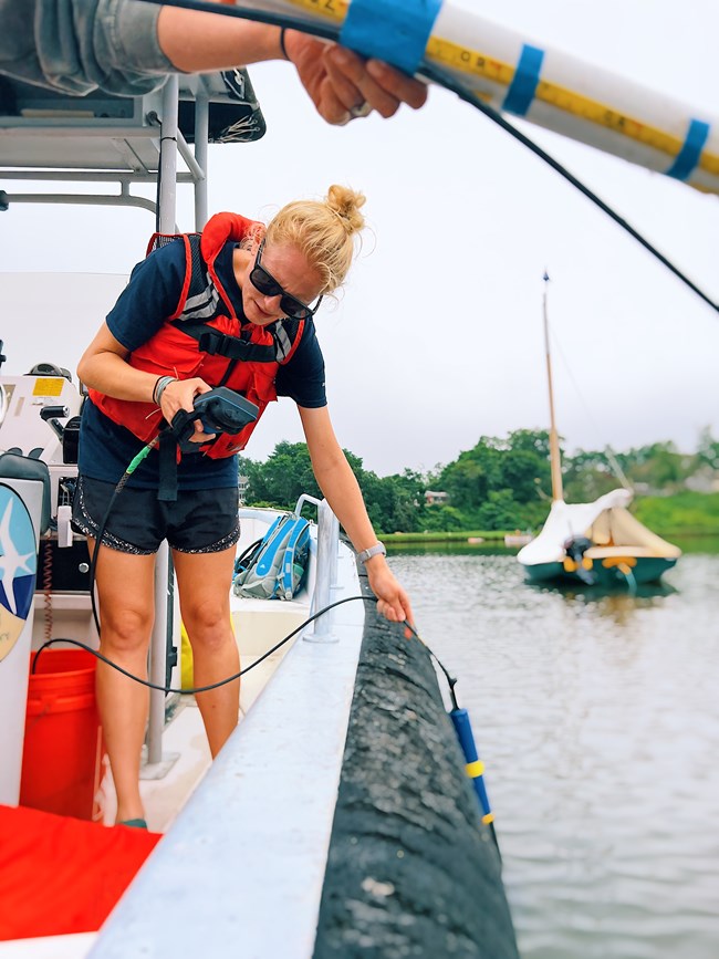 Scientist holds equipment off the edge of a boat to collect temperature data.