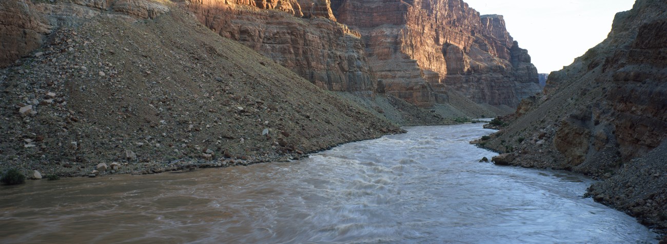 A brownish river runs through rugged canyon walls