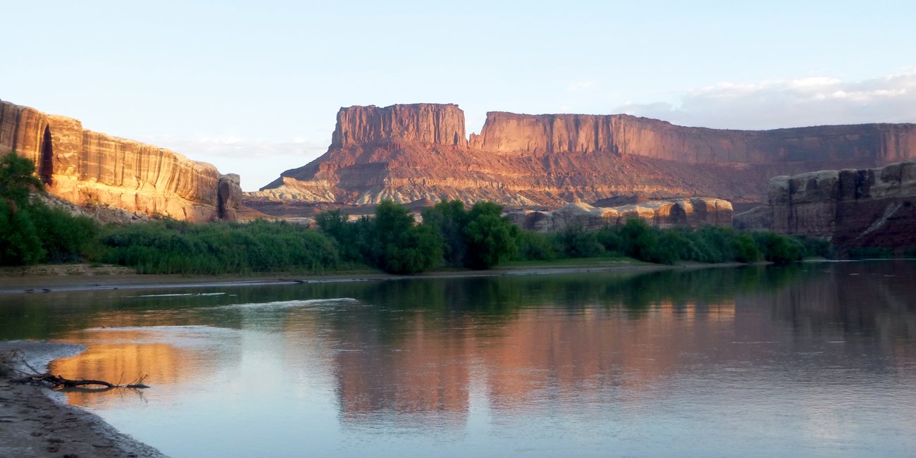 Red rock formations are reflected in a slow-moving river