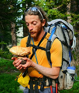 Man wearing backpack looking at large mushroom