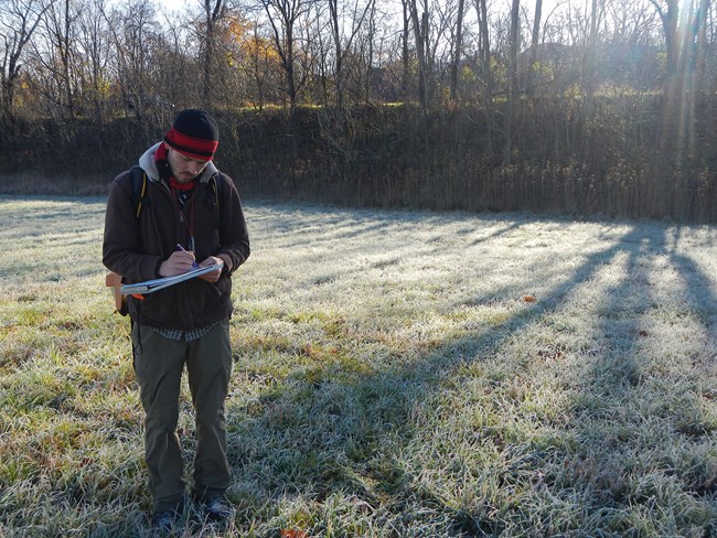Standing in a frosty field, a man records landscape surroundings