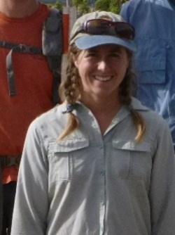 Smiling woman in field clothes standing among fellow crew members.