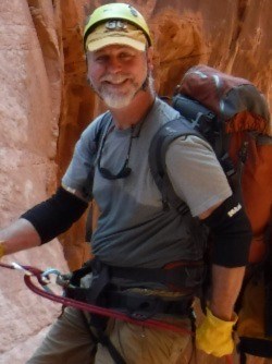 Smiling man with large backpack repelling down a rock wall.