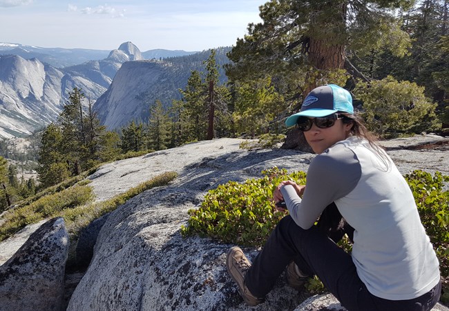 Sarah Wakamiya, Data Manager Woman sitting on granite outcrop, looking back at camera. Views of large granite domes in background.