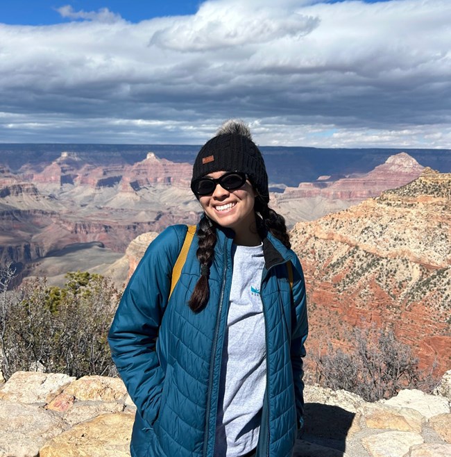 Woman wearing warm hat and coat stands near a view of the redrock cliffs in Grand Canyon National Park