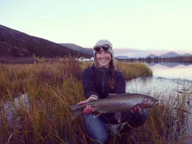 Kelly Martin A woman with a beanie and sunglasses holds a large colorful fish