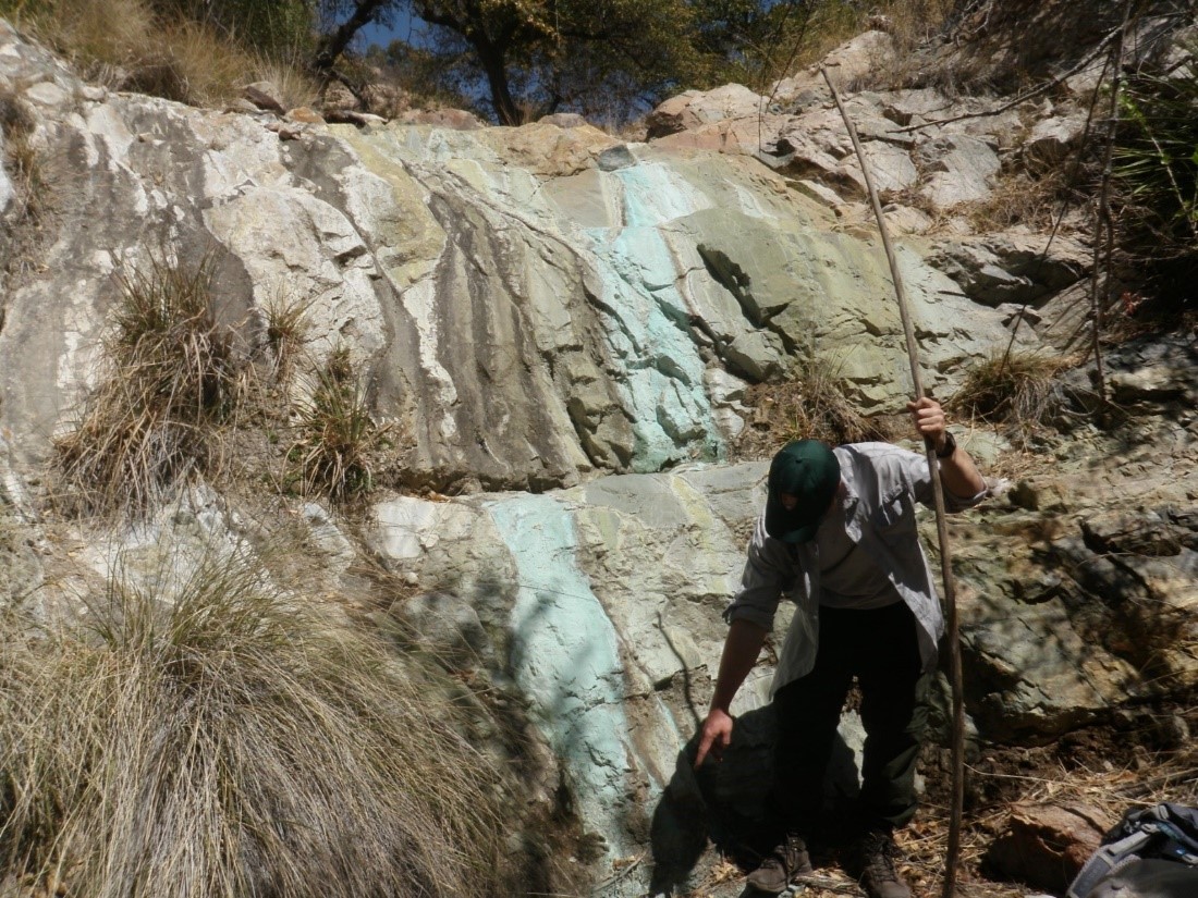  Person stands in front of blue-colored rock ledge.