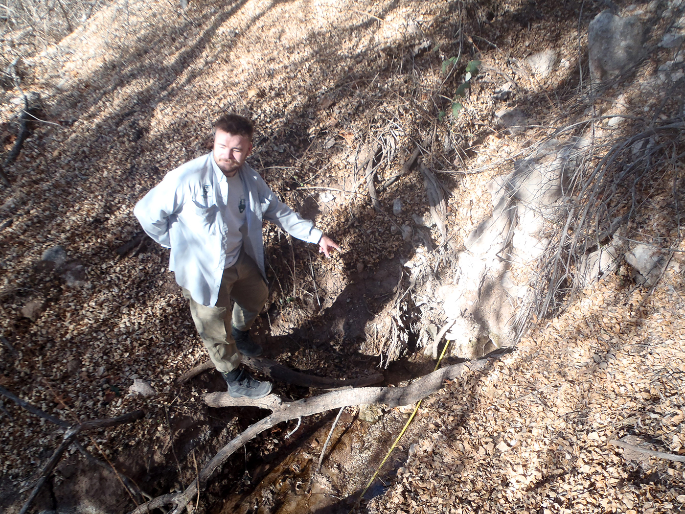 Man points down at water flowing from the base of a rock outcrop.