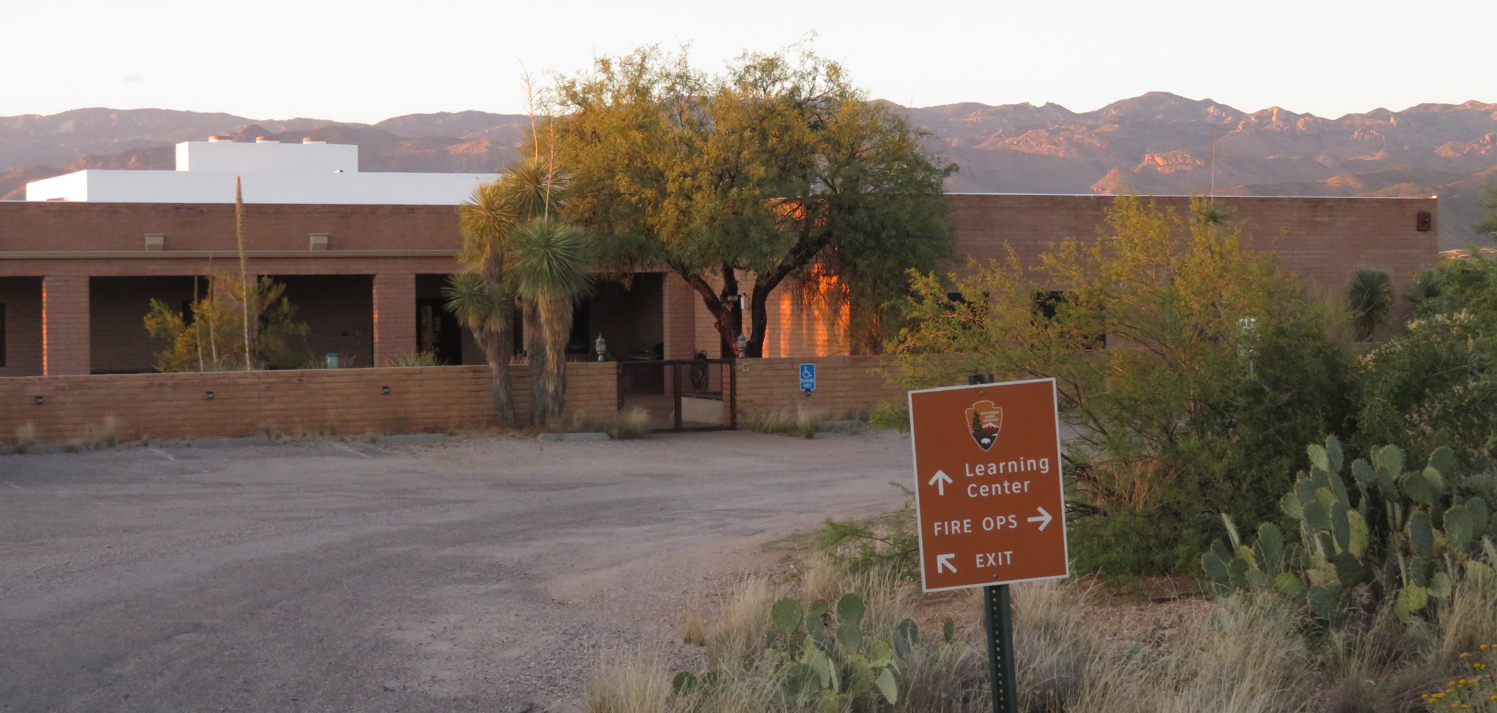 Low brick building, desert mountains in background. Sign with NPS arrowhead reads, Learning Center.