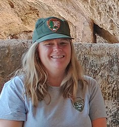 Smiling woman wears NPS ballcap in cliff dwelling