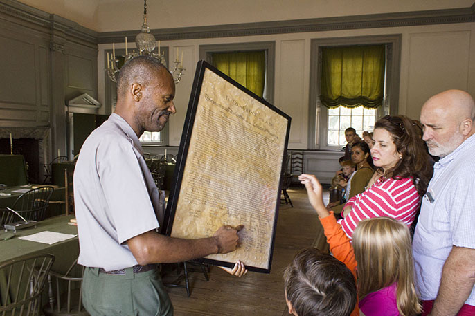 National Park Service Ranger talks to visitors while showing a copy of the Declaration of Independence.