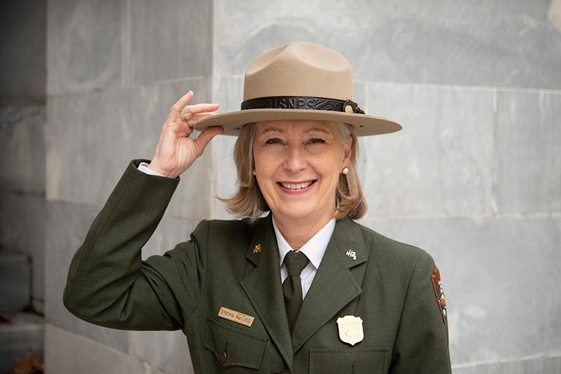 A person wearing NPS green and gray uniform with hand on flat hat.