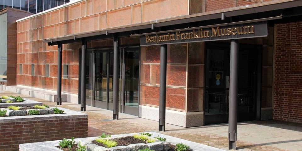 Color photo of a glass and brick building with a sign that says Benjamin Franklin Museum.